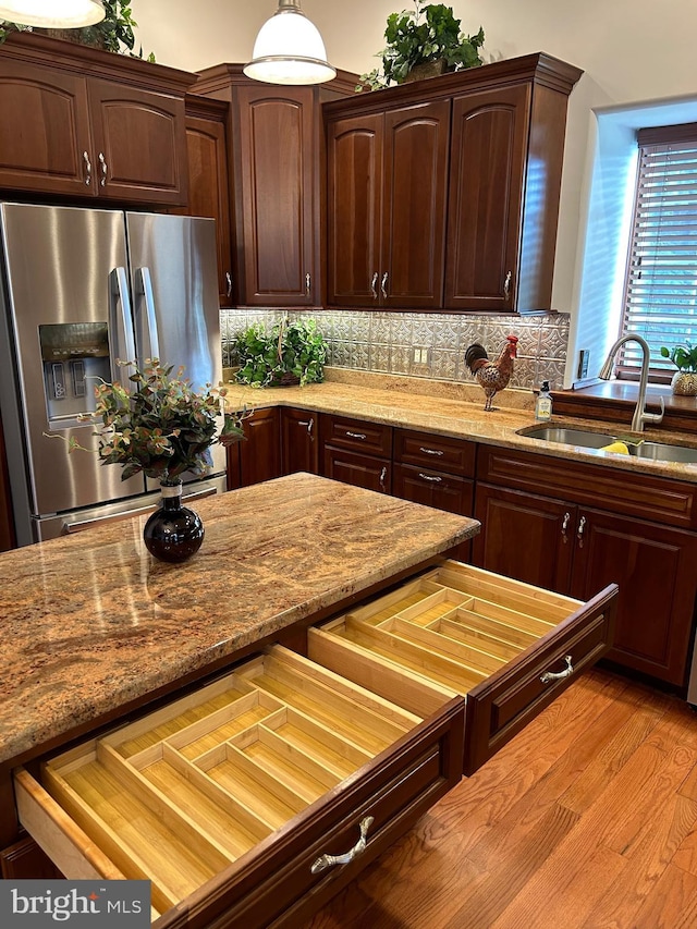 kitchen with sink, hanging light fixtures, stainless steel refrigerator with ice dispenser, backsplash, and light hardwood / wood-style floors