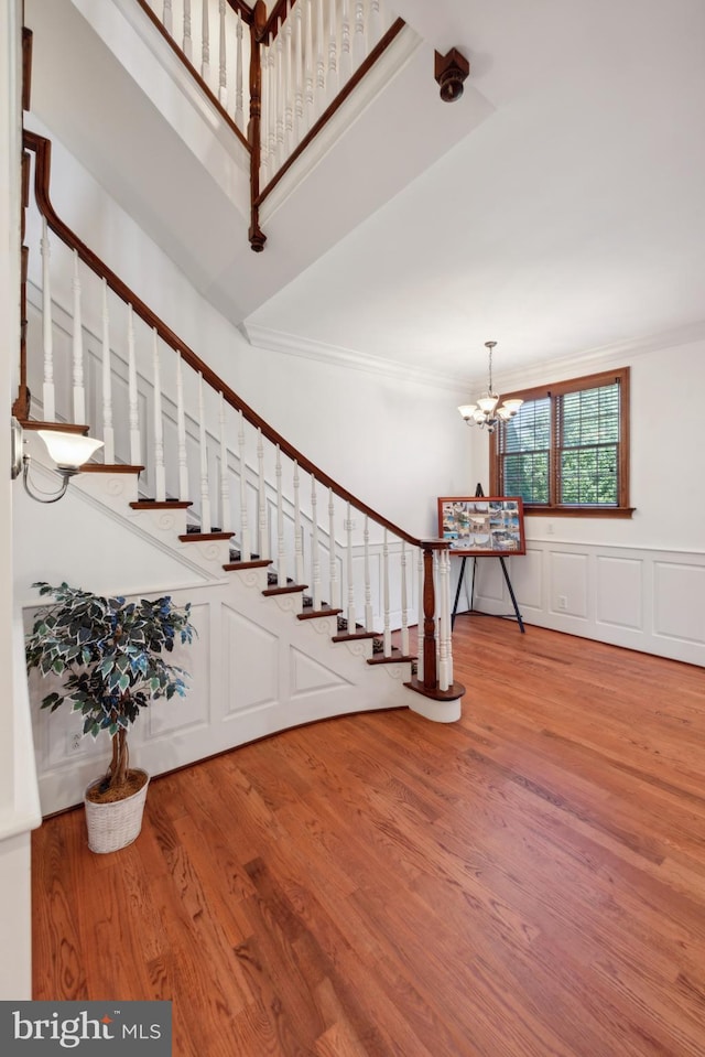 stairs with hardwood / wood-style floors, crown molding, and a notable chandelier