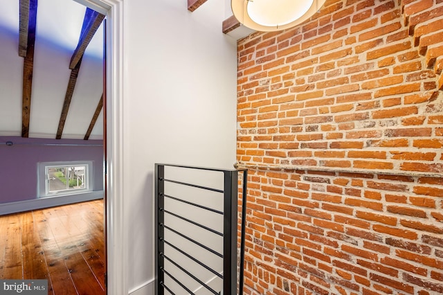 interior space with vaulted ceiling with beams, wood-type flooring, and brick wall