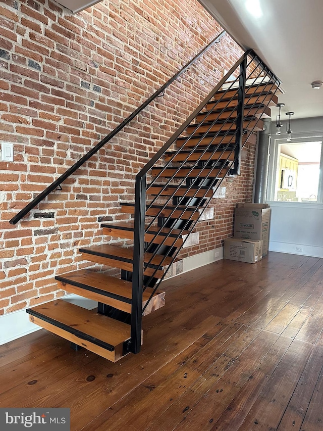 stairway featuring hardwood / wood-style floors and brick wall