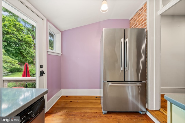 kitchen featuring brick wall, stainless steel appliances, vaulted ceiling, and light hardwood / wood-style flooring