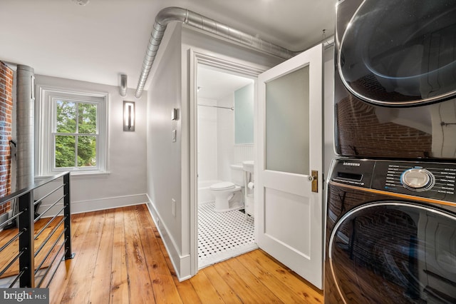 washroom with light hardwood / wood-style flooring, stacked washer / drying machine, and brick wall