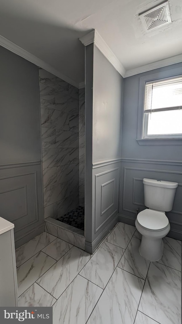 bathroom featuring a tile shower, vanity, toilet, and crown molding