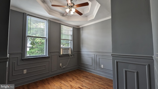 empty room with ceiling fan, a raised ceiling, cooling unit, hardwood / wood-style flooring, and ornamental molding