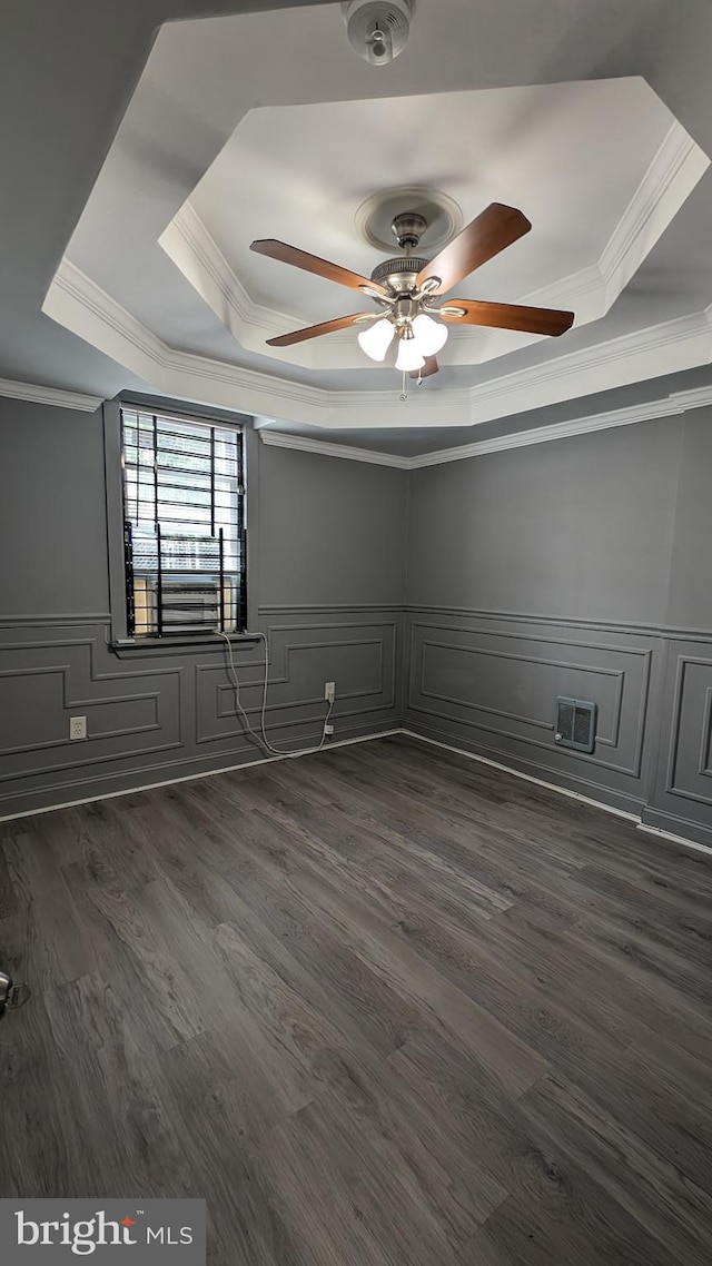 empty room featuring ceiling fan, a raised ceiling, ornamental molding, and dark wood-type flooring