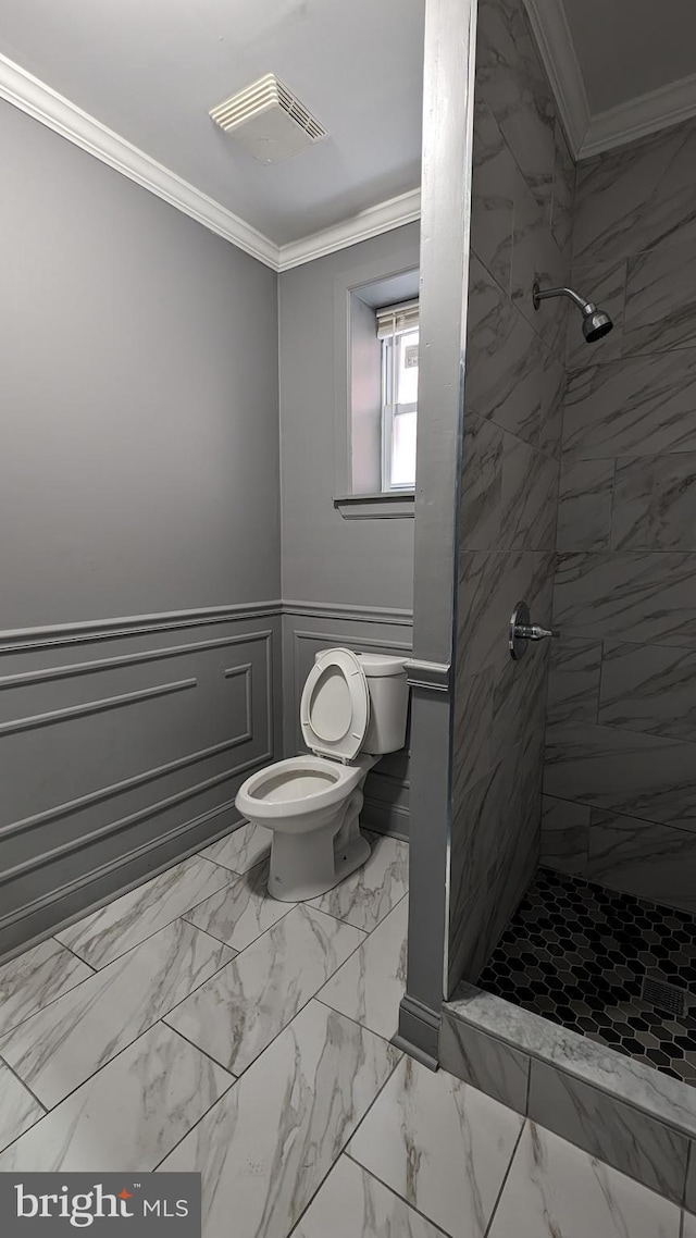 bathroom with a tile shower, toilet, and ornamental molding