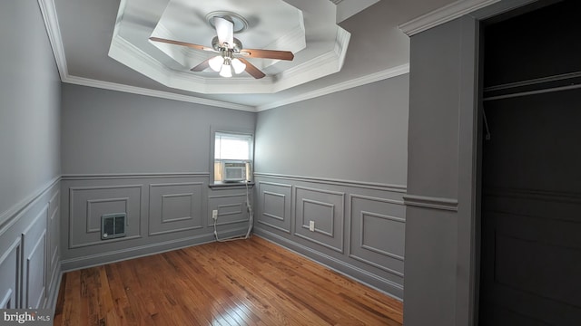 empty room featuring hardwood / wood-style flooring, ceiling fan, a raised ceiling, and ornamental molding