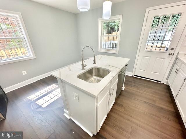 kitchen featuring dishwasher, a kitchen island with sink, white cabinets, sink, and hanging light fixtures