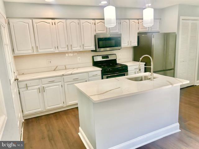 kitchen featuring appliances with stainless steel finishes, sink, pendant lighting, a center island with sink, and white cabinets