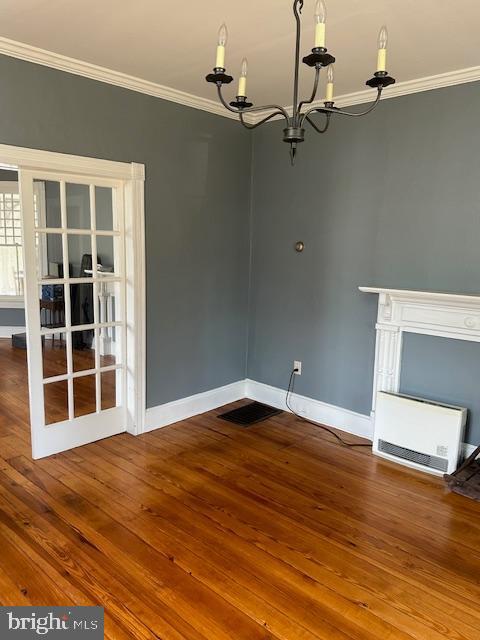 unfurnished dining area with hardwood / wood-style floors, crown molding, and an inviting chandelier