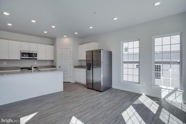 kitchen featuring light stone countertops, light wood-type flooring, stainless steel appliances, and white cabinetry