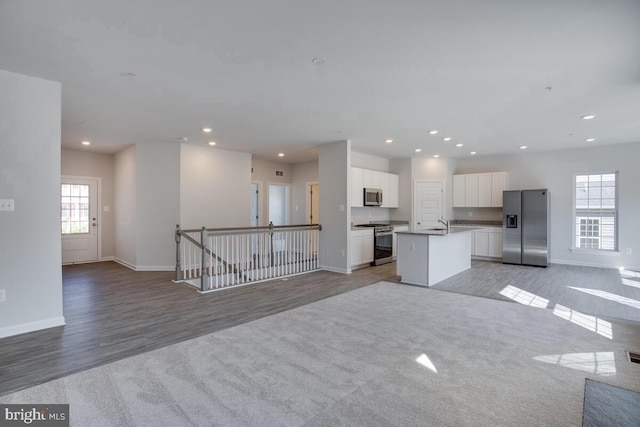 kitchen with stainless steel appliances, white cabinetry, a healthy amount of sunlight, and an island with sink