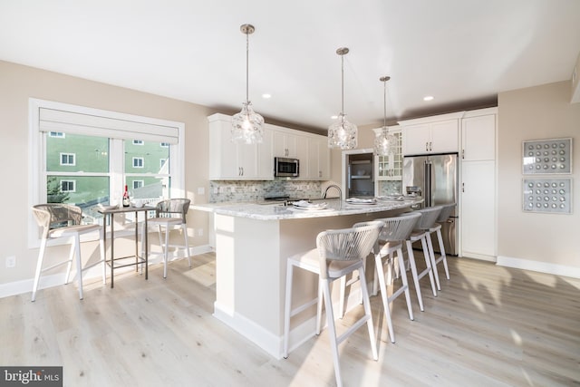 kitchen with white cabinetry, light stone counters, decorative light fixtures, a center island with sink, and appliances with stainless steel finishes