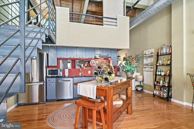 kitchen with hardwood / wood-style floors, a towering ceiling, stainless steel appliances, and sink