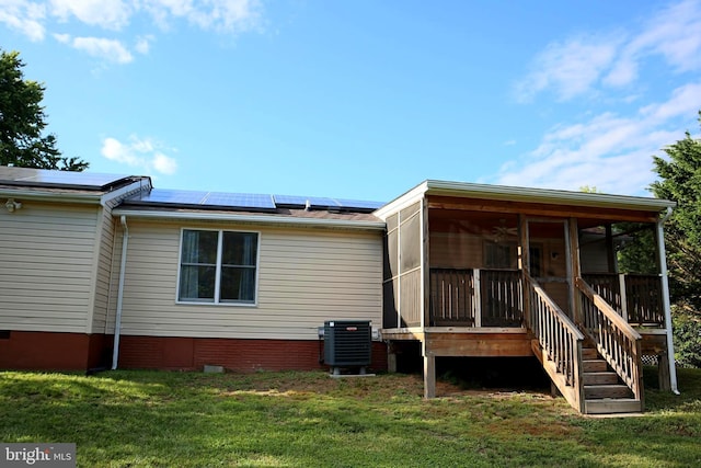 rear view of house with a lawn, a sunroom, cooling unit, and solar panels