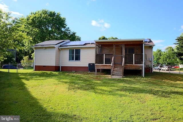 back of property with a sunroom, solar panels, and a yard