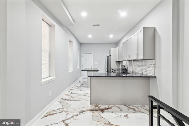 kitchen with stainless steel refrigerator, kitchen peninsula, tasteful backsplash, and sink