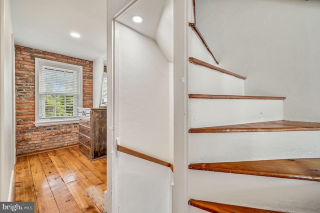 stairway with wood-type flooring and brick wall