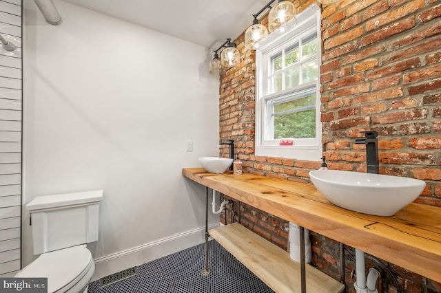 bathroom with sink, brick wall, and toilet