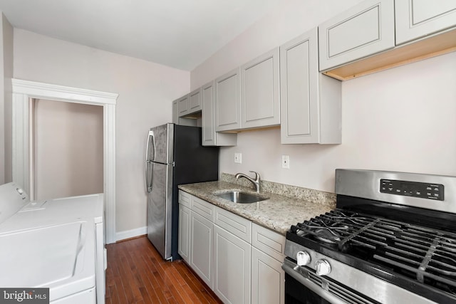 kitchen with light stone counters, stainless steel appliances, dark wood-type flooring, sink, and washing machine and dryer