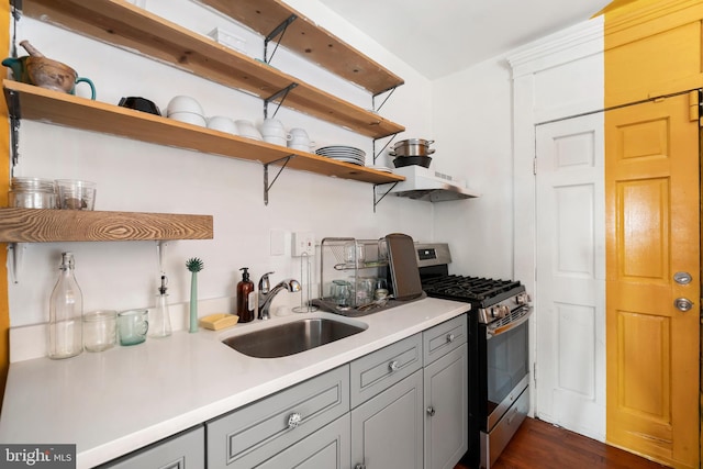 kitchen with gray cabinetry, dark wood-type flooring, exhaust hood, sink, and stainless steel gas range