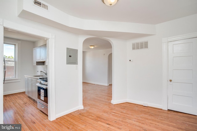 kitchen with white cabinetry, sink, stainless steel range oven, electric panel, and light wood-type flooring