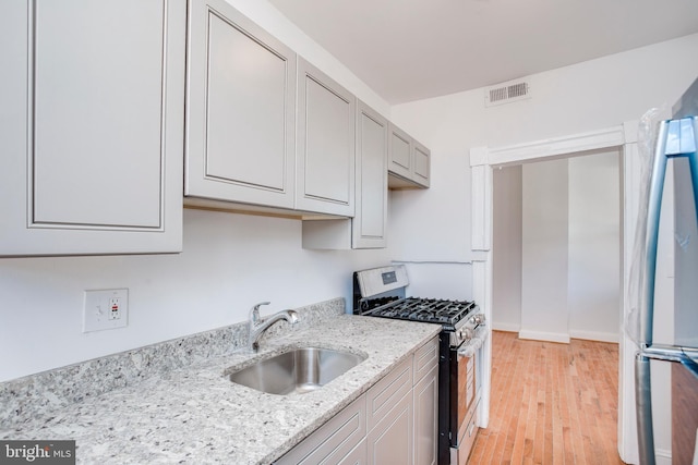 kitchen with sink, stainless steel gas range, light stone counters, light hardwood / wood-style flooring, and refrigerator