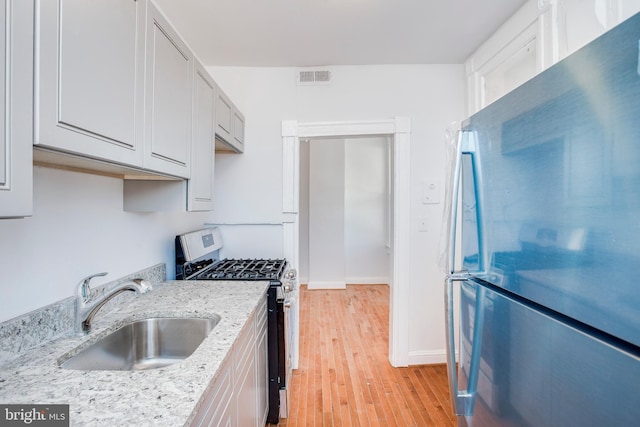 kitchen with light stone countertops, stainless steel gas stove, white cabinetry, and sink