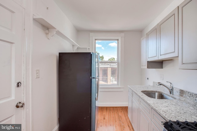 kitchen featuring light stone counters, sink, light hardwood / wood-style flooring, range, and fridge