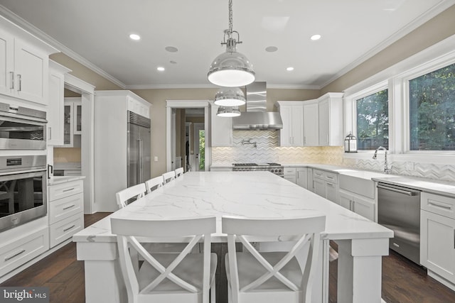 kitchen featuring wall chimney exhaust hood, a kitchen bar, sink, white cabinetry, and stainless steel appliances