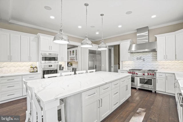 kitchen with wall chimney exhaust hood, high end appliances, white cabinetry, a kitchen breakfast bar, and an island with sink