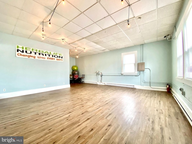 spare room with a wealth of natural light, hardwood / wood-style floors, a baseboard radiator, and a drop ceiling