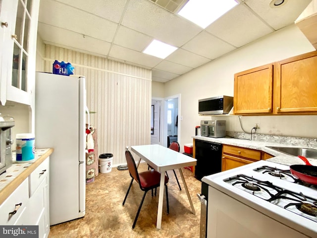 kitchen featuring white refrigerator, light tile flooring, stove, a drop ceiling, and sink