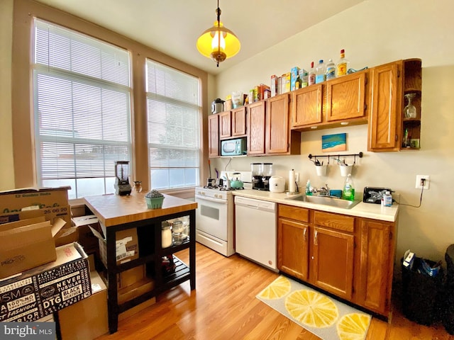 kitchen with white appliances, sink, light hardwood / wood-style floors, and decorative light fixtures