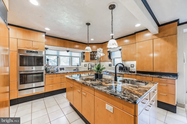 kitchen featuring sink, stainless steel double oven, dark stone counters, a kitchen island with sink, and black electric stovetop