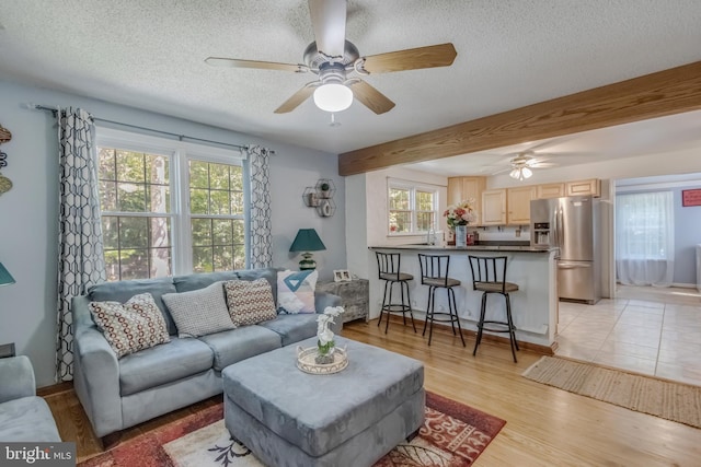 living room featuring ceiling fan, beamed ceiling, a textured ceiling, and light wood-type flooring