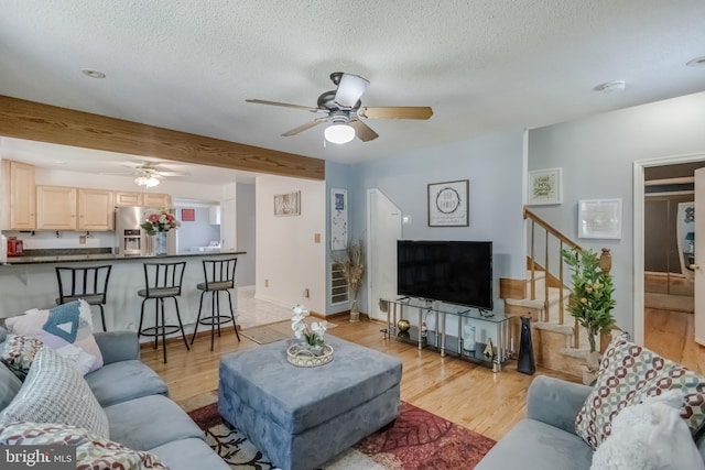 living room featuring beamed ceiling, a textured ceiling, light hardwood / wood-style floors, and ceiling fan