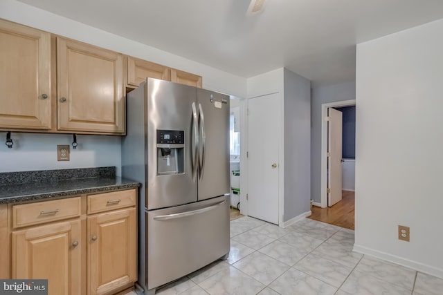 kitchen with stainless steel fridge, light brown cabinetry, light tile patterned flooring, and dark stone counters