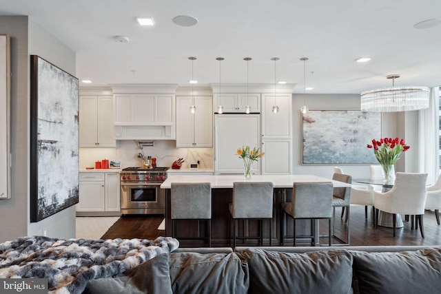 kitchen with white refrigerator, hardwood / wood-style floors, pendant lighting, luxury stove, and a center island with sink