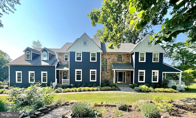 view of front of property featuring board and batten siding, a front lawn, stone siding, and roof with shingles