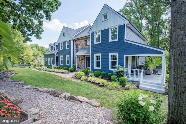 view of front of property with fence, a porch, a front lawn, stone siding, and board and batten siding