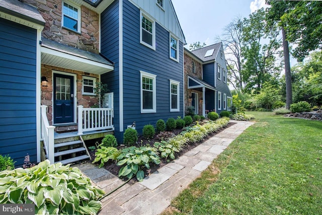 view of side of property featuring covered porch, a lawn, board and batten siding, and stone siding