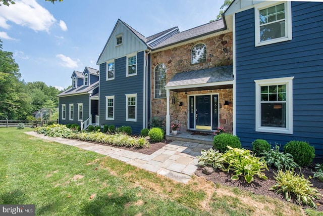 view of front facade featuring a front lawn, fence, board and batten siding, and stone siding