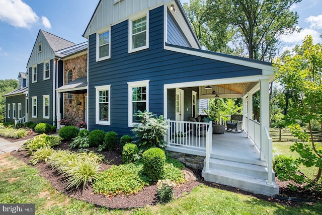 rear view of house featuring stone siding, covered porch, board and batten siding, and fence