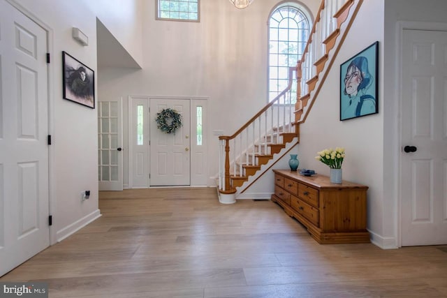 foyer entrance featuring stairway, light wood-style flooring, a high ceiling, and baseboards