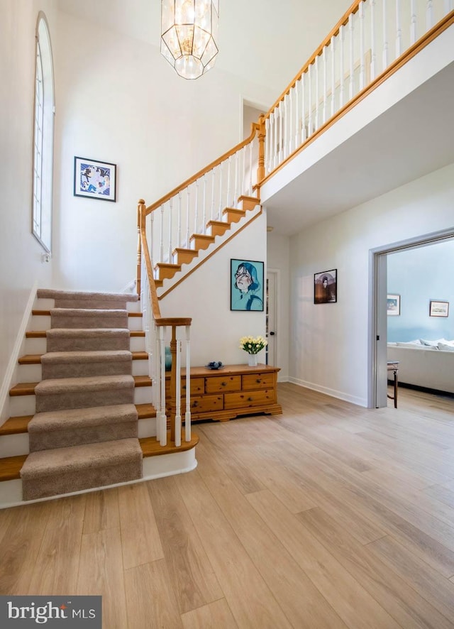 stairway featuring an inviting chandelier, wood finished floors, baseboards, and a towering ceiling