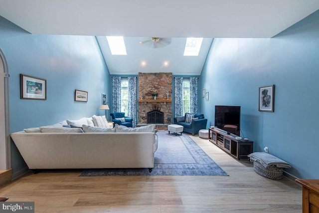 living room with wood finished floors, high vaulted ceiling, a stone fireplace, and a skylight