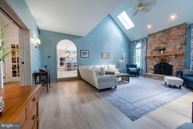 living room featuring wood finished floors, a fireplace, arched walkways, and high vaulted ceiling