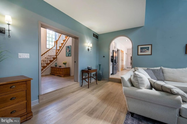 living room featuring baseboards, visible vents, arched walkways, stairs, and light wood-type flooring