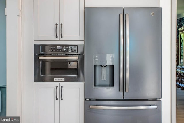 kitchen with wall oven, stainless steel fridge, and white cabinets